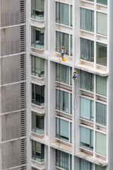 Two men working at height in a high-rise condo in Asia wearing safety harness and wearing helmets