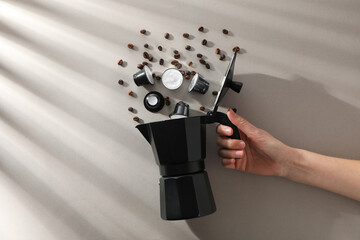 Coffee capsules and beans, coffee maker in hand on gray background, top view