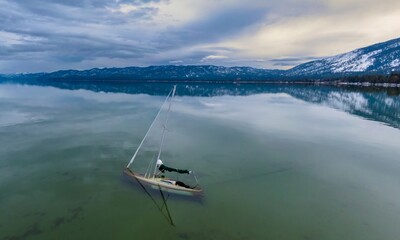 Sunken abandoned yatch and forest mountains with snow. Tahoe Keys, South Lake Tahoe, California,...