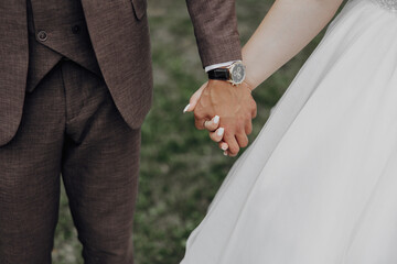 A man and woman are holding hands in a grassy field. The man is wearing a suit and a watch