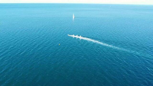 Motorboat tows sailboats on calm clear blue sea. Aerial camera push.