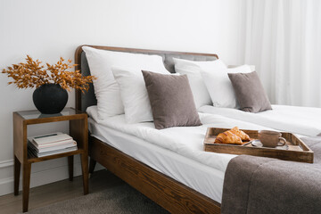 Wooden tray with morning coffee, croissant and flower on bed in luxury hotel bedroom