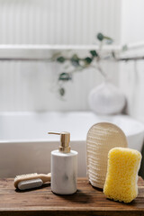Soap dispenser bottle, bath sponges and pumice stone on wooden bench against bathtub