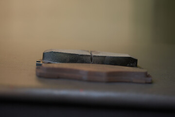 Comparison close up of old and new car brake pads atop a carbon fiber and red-painted car hood.