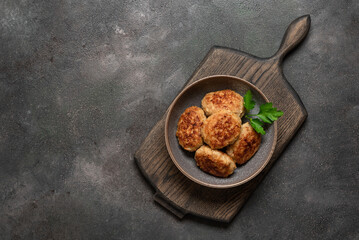 Fried meat cutlets in a bowl on a wooden cutting board, dark rustic background. Top view, flat lay, copy space.