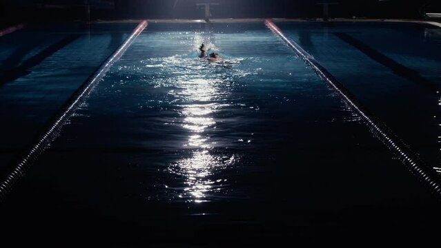 Man swimming backstroke in a swimming pool at night