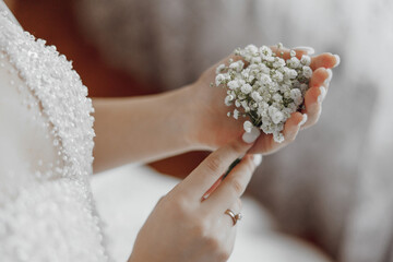 A woman is holding a bouquet of white flowers in her hand. The flowers are small and delicate, and...