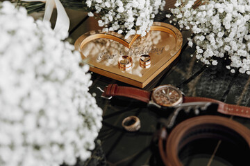 A heart-shaped box with two rings inside and a watch on top. Concept of love and commitment