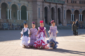 Four girls dancing flamenco, walking, in typical flamenco dress in a nice square in Seville. Dance concept, flamenco, typical Spanish, Seville, Spain.