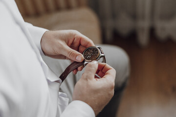 A man is wearing a watch and adjusting it. The watch is brown and has a silver band