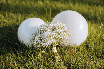 A white flower bouquet is placed on the grass next to two white balloons. Concept of celebration...