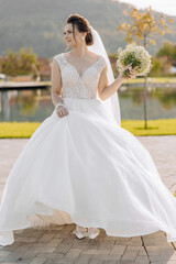 A woman in a white wedding dress is holding a bouquet of white flowers. She is standing on a brick...