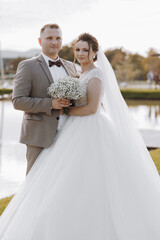 A bride and groom are posing for a picture in front of a body of water. The bride is holding a...