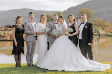 A group of people are posing for a photo, including a bride and groom. The bride is wearing a white...