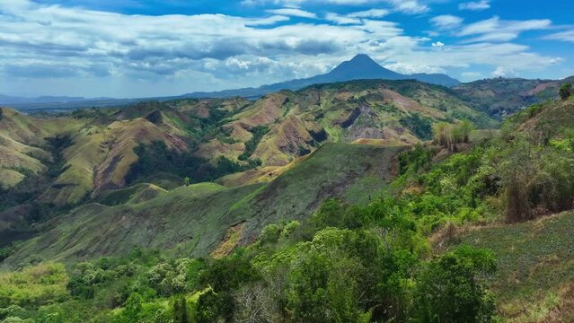 Idyllic drone shot showing green nature hills of southern Mindanao in province of South Cotabato, Philippines. symmetrical Matutum stratovolcano in background. Establishing shot.