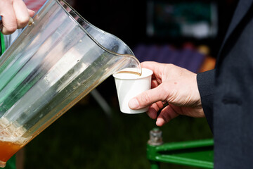 two people hands pouring cider from a plastic jug  into a paper cup