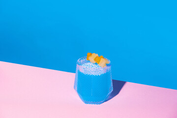 Sweet and sour blue tropical cocktail with pineapple slice against pink blue background....