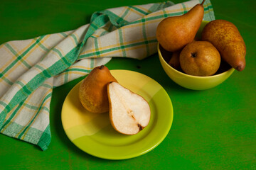 Green plate with whole and half of pear and green kitchen towel on green wooden background..