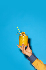 Male hand holding sweet and sour cocktail with orange juice and rosemary against blue background. Concept of alcohol and non-alcohol drink, party, holidays, bar, mix. Poster. Copy space for ad - obrazy, fototapety, plakaty