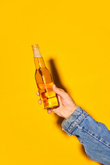 Human hand holding bottle with lager beer against bright yellow background. Concept of alcohol and non-alcohol drink, party, holidays, bar, mix. Poster. Copy space for ad - obrazy, fototapety, plakaty