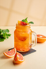 Freshly squeezed blood orange juice with ice, mint and a slice of fruit in a jar on a yellow...
