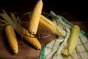 Several cobs sweet corn with green leaves on wooden background..