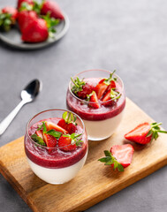 Strawberry and cream panna cotta in glasses with fresh berries on a wooden board on a gray background.