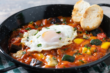 Vegetable pisto manchego with tomatoes, zucchini, peppers, onions,eggplant and egg, served in frying pan on wooden table. Close up