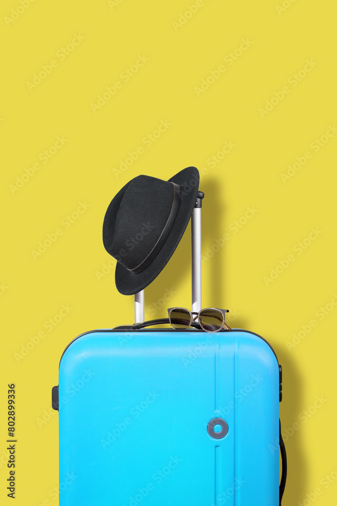 Wall mural blue suitcase and black hat on a yellow background.