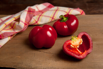 Two whole and halves of red bell pepper on wooden background with red kitchen towel. .