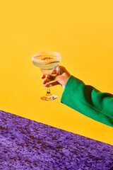 Female hand holding sweet and sour margarita cocktail with slice of orange against bright yellow background. Concept of alcohol and non-alcohol drink, party, holidays, bar. Poster. Copy space for ad - obrazy, fototapety, plakaty