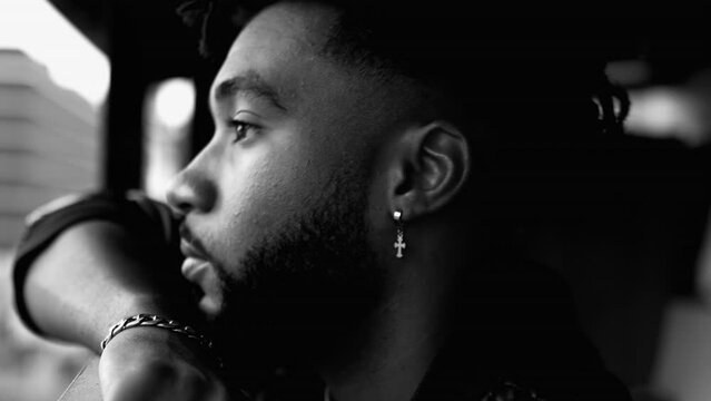 Profile close-up face of a contemplative young black man with deep pensive emotion. 20s person reflecting about life during challenging times in intense monochromatic, black and white