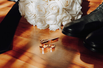 A man's wedding ring and tie are on a table next to a bouquet of white roses