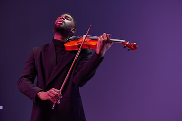 A skilled musician in elegant attire showcasing his talent with a violin against a vibrant purple...