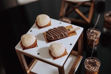 A dessert table with a variety of desserts including a chocolate covered ice cream stick. The desserts are arranged on a white tray with a gold frame