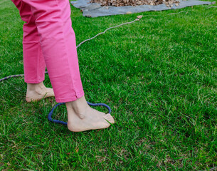 Shot with a close-up on the feet of a Caucasian woman walking barefoot: she tries to grab a ring of blue rope resting on the grass with just her feet. Nice sunny day