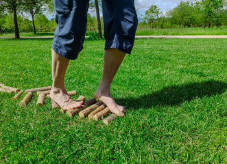 Shot with a close-up on the feet of a Caucasian man walking barefoot: he walks on small trunks arranged horizontally, it is a stretch of path in nature. Nice sunny day.