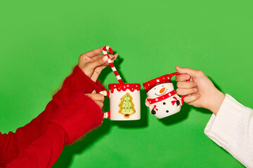 Hands holding mugs decorated in Christmas theme against green background. Hot tea, cocoa and hot chocolate. Concept of drink, party, holidays. Poster. Copy space for ad