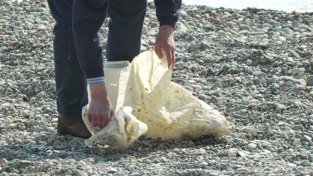 Garbage on beach - Elder Man collects garbage on beach after storm, maintaining cleanliness and preserving environment.