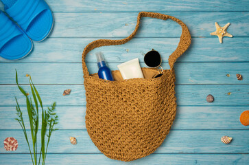 Beach bag with things on a blue wooden background. Top view, copy space