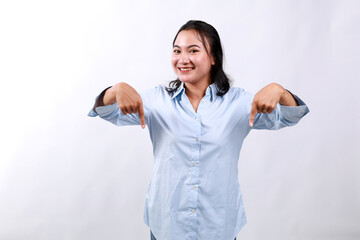 Portrait of young asian woman standing pointing fingers down and smiling, showing banner, click on...