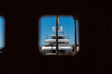 Blick durch ein Loch in einer Mauer auf eine Luxusyacht im Hafen von Tarragona, Spanien