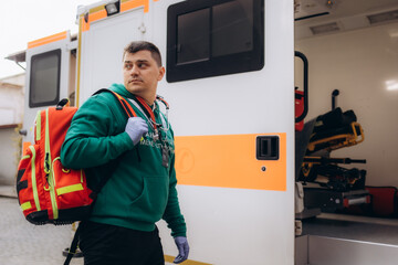 A male paramedic in uniform stands with his arms crossed in front of an ambulance and his colleague...