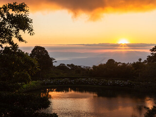 Obraz premium High angle view of small lake in hilly terrain with reflection of the setting sun and the Pacific Ocean in the background, Monteverde, Costa Rica