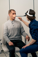 in the clinic young doctor in blue ear throat nose examines the patient s throat