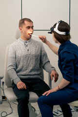 in the clinic young doctor in blue ear throat nose examines the patient s throat