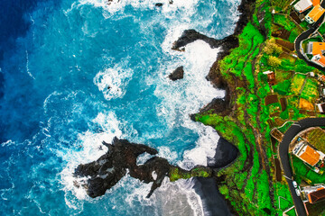 Aerial view of rough ocean with waves, volcanic beach and swiming pool in Seixal, Madeira, Portugal