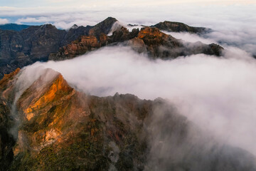 Aerial view of majestic mountain ridges at sunrise with falling fog from top of Pico do Areeiro, Madeira island, Portugal