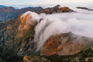 Aerial view of majestic mountain ridges at sunrise with falling fog from top of Pico do Areeiro, Madeira island, Portugal