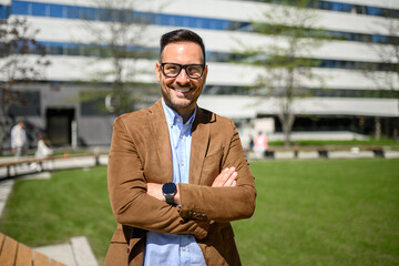 Portrait of confident businessman in eyeglasses and arms crossed standing against lawn and building